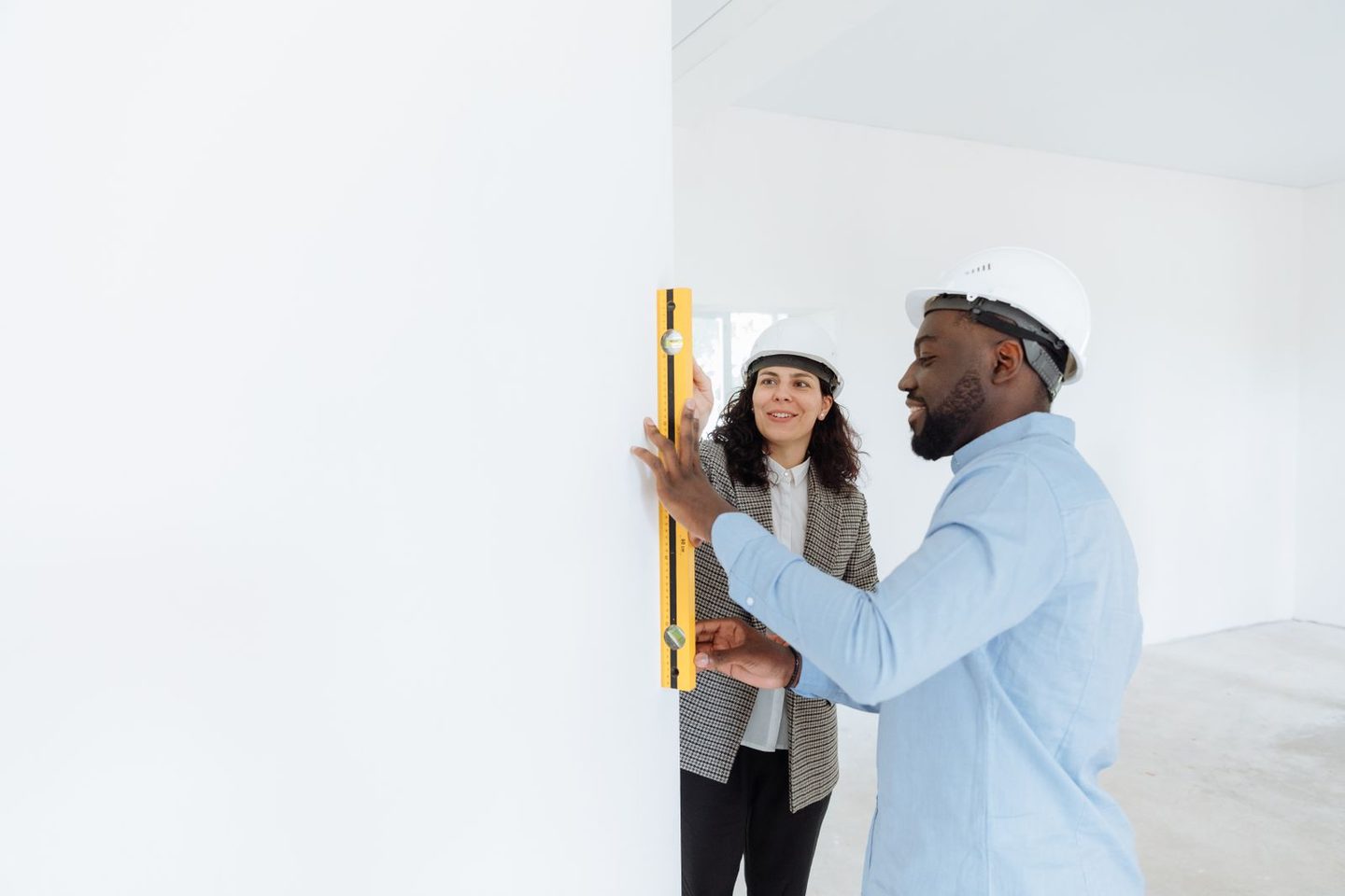 Twee vakmensen met bouwhelm controleren een muur met een waterpas bij een renovatie
