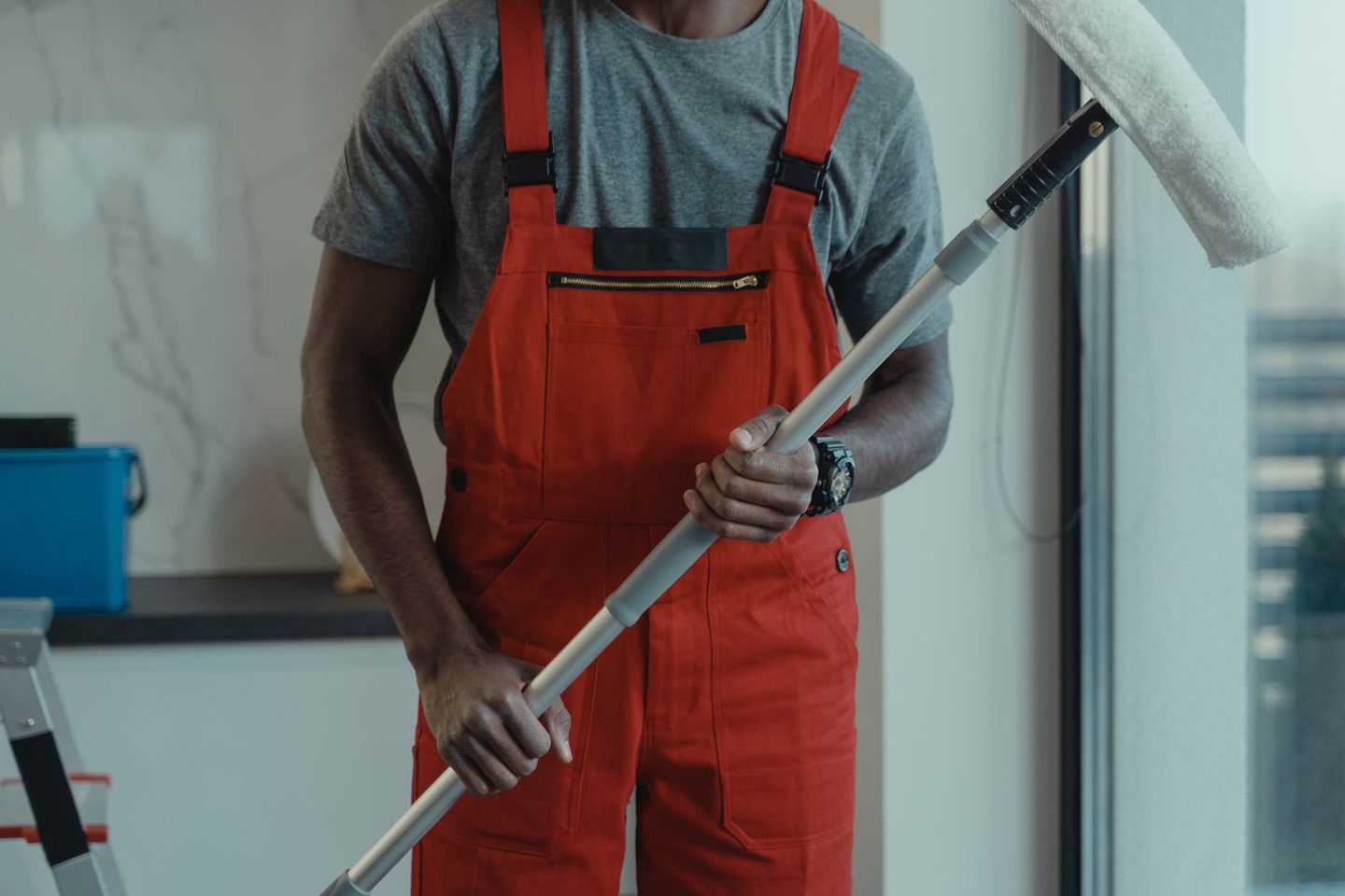 Schoonmaker in overall met een lange steel voor het wassen van ramen en gevels